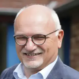 Eckhard Lueling, ein Mann mit Brille und grauem Bart, lächelt in einem blauen Anzug.