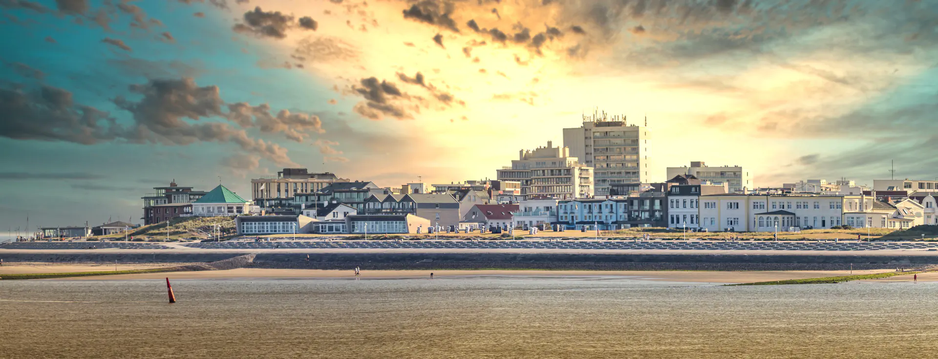 Panorama von Norderney mit Strand, Promenade und Gebäuden unter dramatischem Himmel.