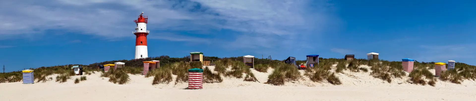 Leuchtturm Borkum mit bunten Strandkörben auf sandiger Düne unter blauem Himmel.