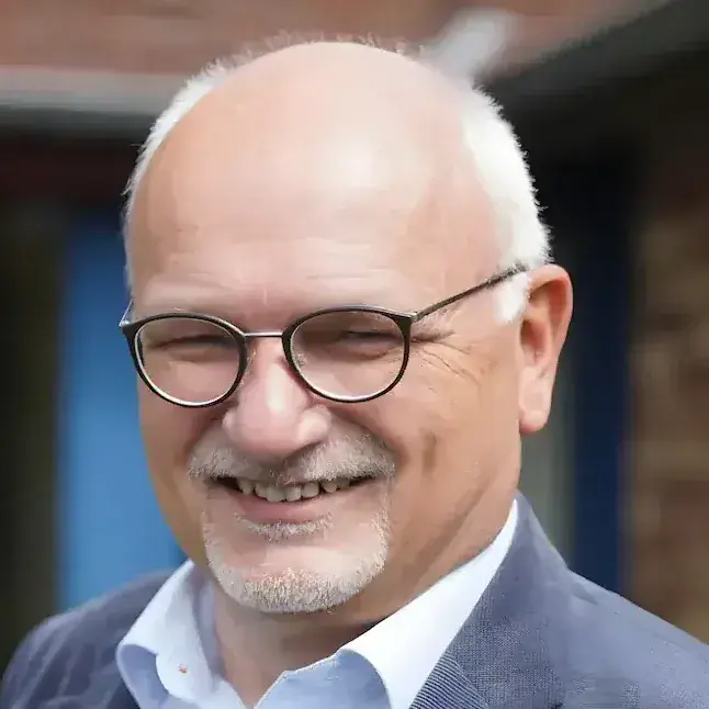 Eckhard Lueling, ein Mann mit Brille und grauem Bart, lächelt in einem blauen Anzug.