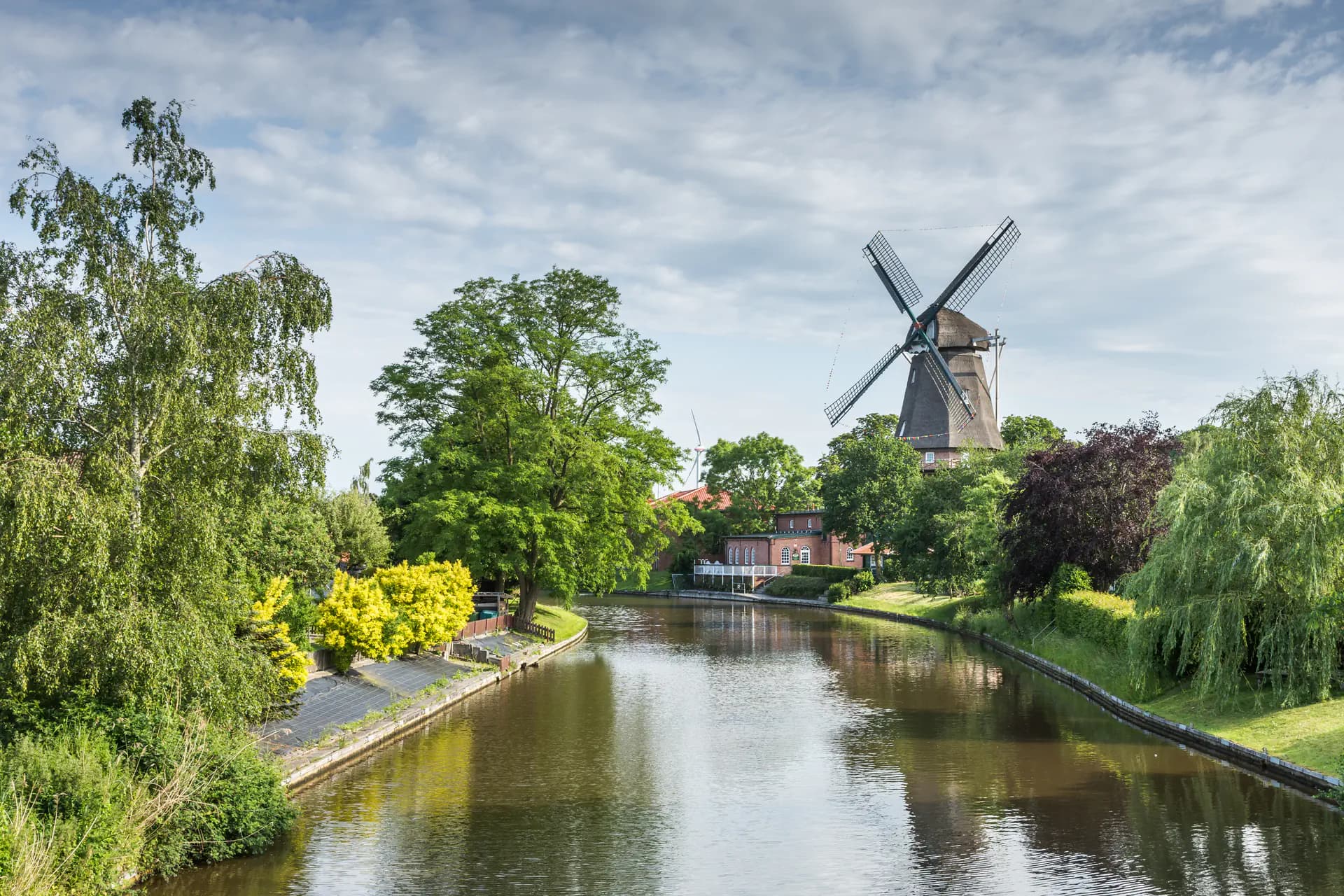 Windmühle am Kanalufer mit Bäumen und Häusern, Emden